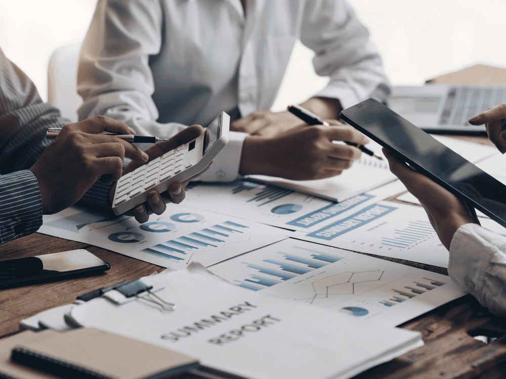 Person with a calculator at a desk with a group looking at finance reports